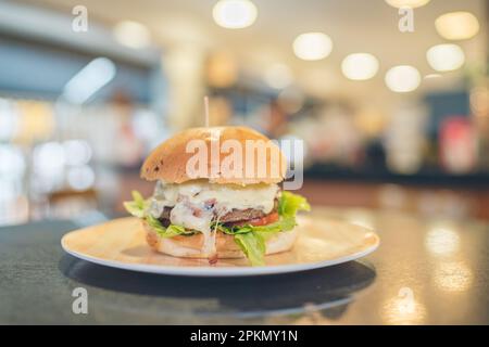 Horizontales Foto von Brot mit Hamburger auf einem Tisch, gefüllt mit Mosarella-Käse, Tomaten und Salat Stockfoto