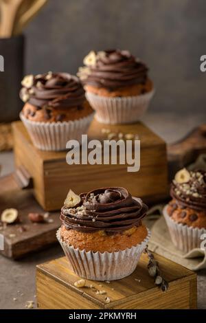 Schokoladenstückchen-Muffins, dekoriert mit Schokoladenganache und Haselnuss auf einer alten dunklen Küchenplatte. Stockfoto
