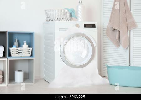 Beim Waschen im Zimmer tritt Schaum aus der defekten Waschmaschine aus Stockfoto