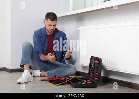 Mann, der Schlüssel in der Nähe des Kastens mit Werkzeugen im Innenbereich wählt Stockfoto