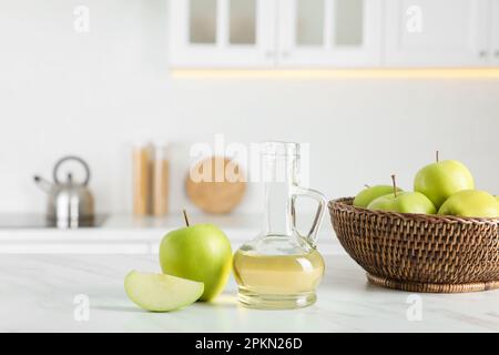 Natürlicher Apfelessig und frisches Obst auf weißem Marmortisch in der Küche Stockfoto