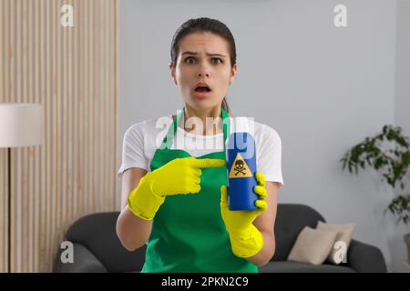 Frau, die eine Flasche giftiger Haushaltschemikalien mit einem Warnschild im Innenbereich vorführt Stockfoto