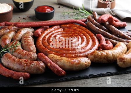 Verschiedene köstliche Würstchen mit Rosmarin und Saucen auf Holztisch, Nahaufnahme. Auswahl an Biersnacks Stockfoto