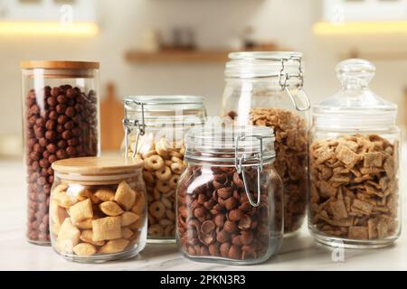 Glasbehälter mit verschiedenen Frühstückszerealien auf einem weißen Marmortisch in der Küche Stockfoto