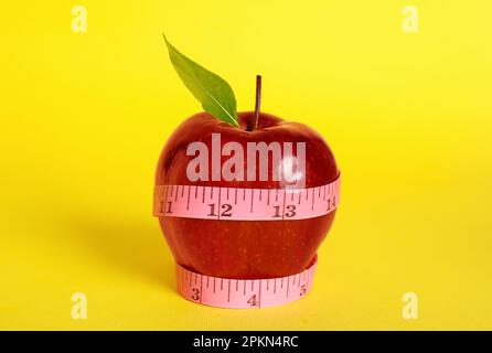 Frischer roter Apfel mit Maßband auf gelbem Hintergrund Stockfoto