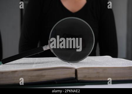Lupe über ein offenes Buch auf dem Tisch. Bildungs- und Forschungskonzept. Stockfoto