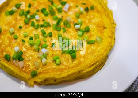 Einfaches Ei-Omelette mit Kräutern auf weißem Teller. Flauschiges Frühstücks-Omelette mit grünen Frühlingszwiebeln. Frühstück mit Spiegeleiern in der Pfanne. Keto ketogene Diät. Stockfoto