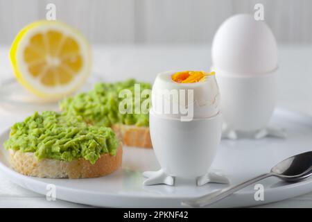 Weich gekochtes Ei und offenes Brot-Sandwich mit Avocado auf dem Tisch. Traditionelles Essen für ein gesundes Frühstück. Stockfoto