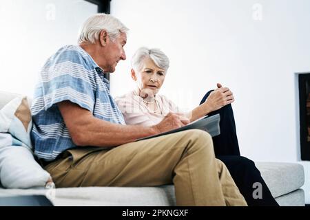 Haben wir genug getan, um unsere finanzielle Zukunft zu sichern? Ein Seniorenpaar, das zu Hause seine Finanzen durchsucht und besorgt aussieht. Stockfoto