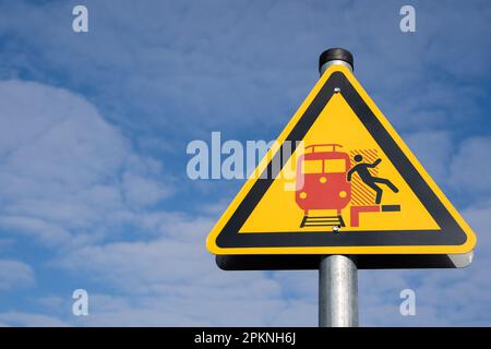 Gelbes dreieckiges Warnschild für Passagiere auf einem deutschen Bahnsteig, d. h. Achtung vor ankommenden und vorbeifahrenden Zügen Stockfoto