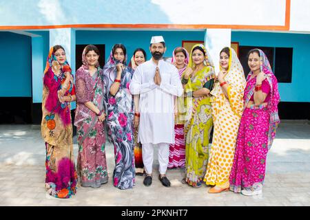 Ein indischer Politiker, der namaste mit einer Gruppe traditioneller Frauen macht. Konzept von Wahl und Abstimmung. Stockfoto