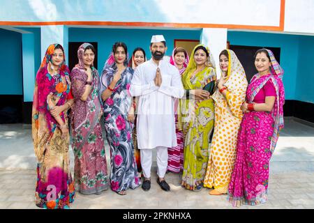 Ein indischer Politiker, der namaste mit einer Gruppe traditioneller Frauen macht. Konzept von Wahl und Abstimmung. Stockfoto