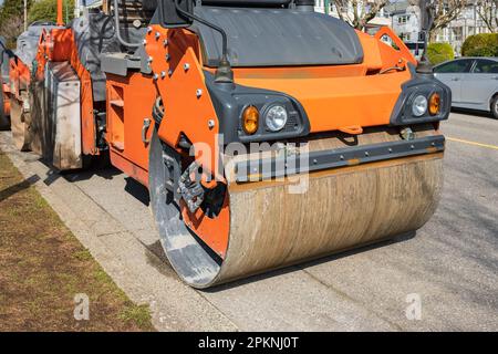 Nahaufnahme der Laufrolle, die auf der neuen Baustelle arbeitet. Seitenansicht der Asphaltwalze. Straßenreparaturarbeiten, Asphaltpflaster. Asphaltverdichter Stockfoto