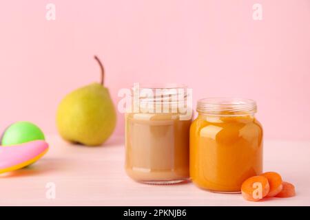 Glasgefäße mit nährstoffhaltiger Babynahrung auf pinkfarbenem Hintergrund. Gemüse- und Obstpüree Stockfoto