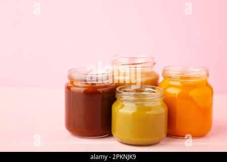 Gläser mit Babypüree auf pinkfarbenem Hintergrund. Draufsicht Stockfoto