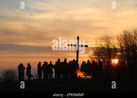 Silhouetten von Menschen versammelten sich am Osterkreuz bei Sonnenaufgang, nachdem sie die Morgenkommunion am Ostertag, dem 9. April 2023, gefeiert hatten. Stockfoto