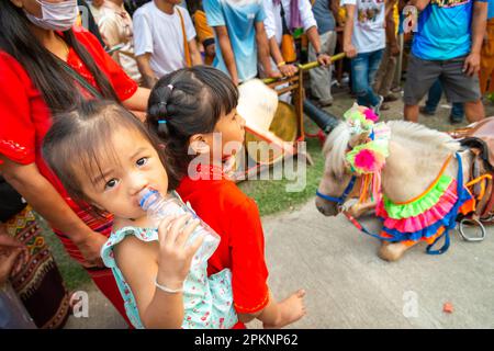 Pai, Nord-Thailand-April 4. 2023: Familien schauen zu, wie ein Pferd, gekleidet in zeremonieller Kleidung zusammenbricht, und wird von einer Frau unterstützt, die ihren großen Hut benutzt Stockfoto