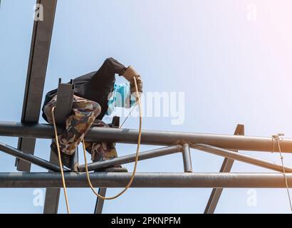 Ein Schweißer, der auf einem hohen Dach für ein neues Gebäude arbeitet. Stockfoto