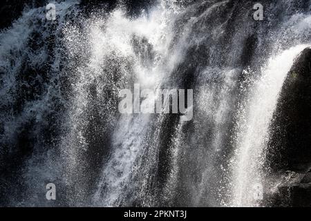 Tropischer Wasserfall mit Wassertropfen und Sprühnebel, die im Sommer von einer Klippe in der Sonne fallen. Hohe Verschlusszeit. Stockfoto