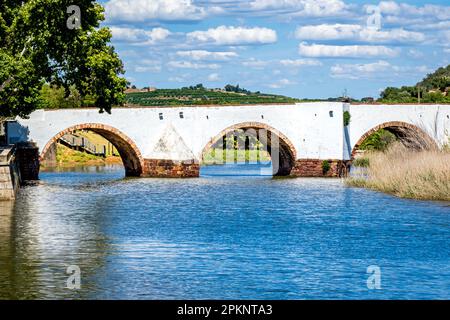 Die antike Ponte Romana de Silves, eine malerische Brücke aus weißem Stein über den friedlichen Fluss Arade im warmen Sonnenlicht am Nachmittag. Stockfoto