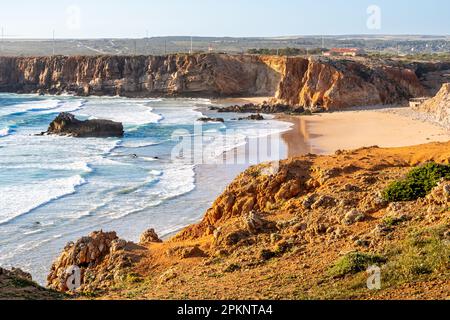 Der idyllische, leere Surfplatz Praia do Tonel Beach wird während der goldenen Stunde in warmes Abendsonnenlicht getaucht, während seichte Wellen sanft gegen das Ufer schlagen. Stockfoto