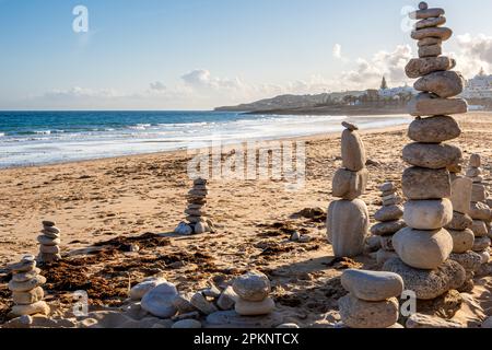 Wenn die Sonne am Strand Praia da Luz untergeht, schaffen genau ausgeglichene Steinhaufen einen künstlerischen Ausdruck von Gleichgewicht und Harmonie. Stockfoto