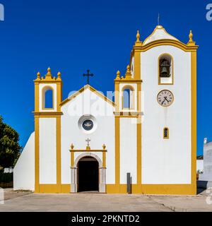 Vorderansicht vom Vorplatz der gelb gerahmten weißen Fassade der Kirche Igreja de Nossa Senhora da Luz mit Glockenturm und Bogeneingang. Stockfoto