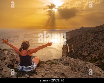 Die Frau sitzt auf den Dingli Cliffs. Es ist eine über 200 Meter hohe Felsformation, die seit Jahrhunderten eine natürliche Verteidigung der maltesischen Küste ist Stockfoto