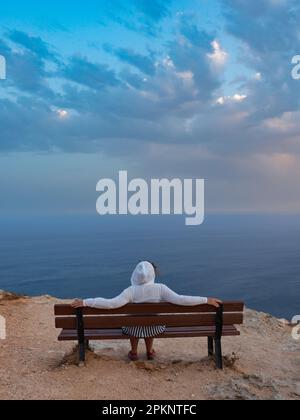 Die Frau sitzt auf der Bank bei den Dingli Cliffs. Es ist eine über 200 Meter hohe Felsformation, die seit Jahrhunderten eine natürliche Verteidigung des Mal ist Stockfoto