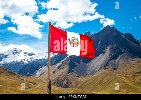 Die peruanische Flagge flattert im Wind vor dem majestätischen Gebirge La Raya mit dem schneebedeckten Gipfel von Chimboya im Hintergrund. Stockfoto