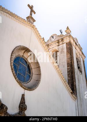 Niedriger Winkel Blick auf die Fassade der Gemeindekirche Monchique, Igreja de Nossa Senhora da Conceição, von der Sonne beleuchtet mit einer Uhr, die fast zwölf anzeigt. Stockfoto
