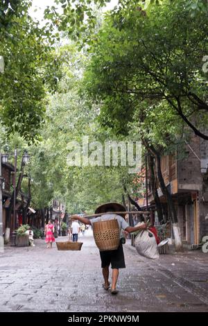 Ein Chinese trägt schwere Säcke auf seinen Schultern, die an einem Bambusstock in Fenghuang, China, befestigt sind. Stockfoto