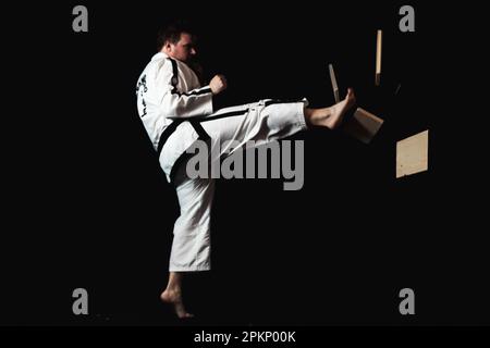 Ein junger Mann führt ein Kampfsportmanöver auf schwarzem Hintergrund durch und demonstriert sein Können in der Kunstform Stockfoto