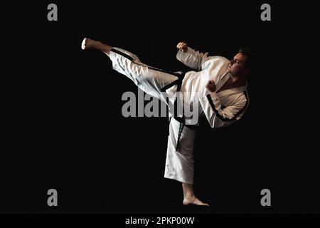 Ein junger Mann führt ein Kampfsportmanöver auf schwarzem Hintergrund durch und demonstriert sein Können in der Kunstform Stockfoto
