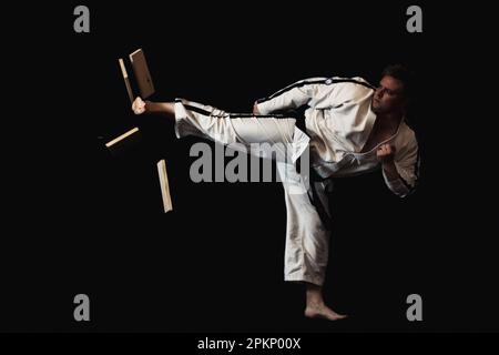 Ein junger Mann führt ein Kampfsportmanöver auf schwarzem Hintergrund durch und demonstriert sein Können in der Kunstform Stockfoto
