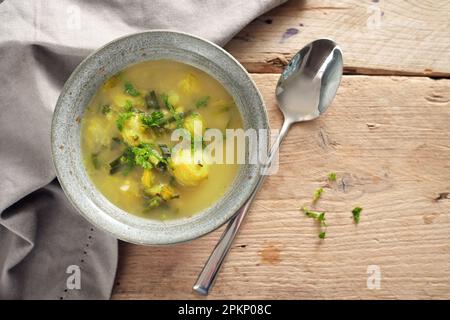 Gemüsesuppe mit rosenkohl, Lauch und Kartoffel in einer Schüssel, Löffel und Serviette auf einem rustikalen Holztisch, Blick aus einem hohen Winkel von oben, Kopierraum, Sel Stockfoto