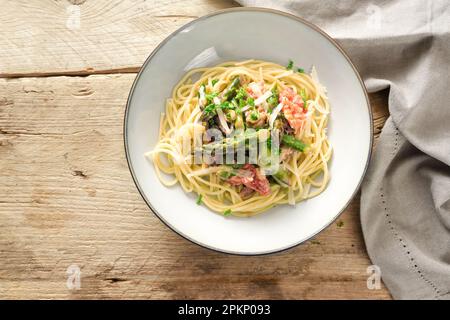 Gemüsesauce aus grünem Spargel und Tomaten mit Parmesan und Petersilie garniert auf Spaghetti auf einem Teller auf einem rustikalen Holztisch, Hochwinkel-Topvie Stockfoto