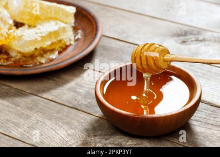 Honig in Schüssel mit Pendelarm und Wabenmuster auf Holztisch Stockfoto