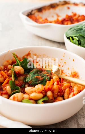 Gesundes Frühstück und Mittagessen, gedünstete weiße Bohnen mit Karotten, Zwiebeln und Tomaten mit Spinatblättern, eine Schüssel Bohnen und Spinat Stockfoto