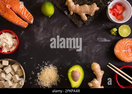 Aufnahme von Zutaten für Sushi über Kopf auf dunklem Hintergrund. Rohes Lachssteak, Reis, Frischkäse, Avocado, Limette, Eingelegter Ingwer (Gari), roher Ingwer war Stockfoto