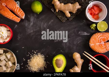 Aufnahme von Zutaten für Sushi über Kopf auf dunklem Hintergrund. Rohes Lachssteak, Reis, Frischkäse, Avocado, Limette, Eingelegter Ingwer (Gari), roher Ingwer war Stockfoto