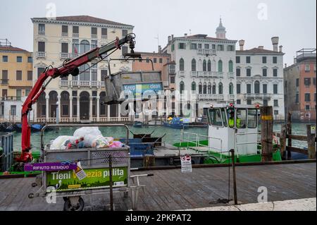 Venedig, Italien - 23. Februar 2023: Abfalleimer gefüllt mit Müll werden auf das Sammelschiff neben dem Canale Grande in Venedig geladen Stockfoto