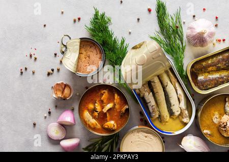 Verschiedene offene Blechdosen mit Fischkonserven unter Gewürzen und Kräutern, Lachs- und Makrelenkonserven, Sprotte und Sardine, Thunfisch und Hering sowie Fischpastete Stockfoto