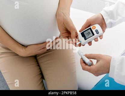 Endokrinologe Kontrolle des Blutzuckerspiegels bei Schwangeren mit Gestationsdiabetes mittels Glukometer in der Klinik während der Sprechstunde. Hohe BL Stockfoto