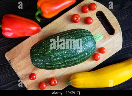 Gemüsemark und süßer Pfeffer auf Holztisch, flach liegend. Draufsicht auf frische Zucchini und Tomaten auf dem Schneidebrett, Set mit Bio-Lebensmitteln. Konzept von Stockfoto