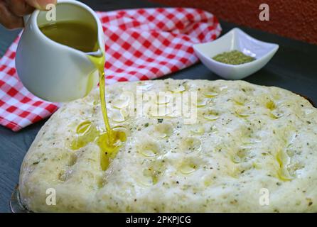 Olivenöl wird vor dem Backen auf die Oberfläche des Focaccia-Brotteigs gegossen Stockfoto