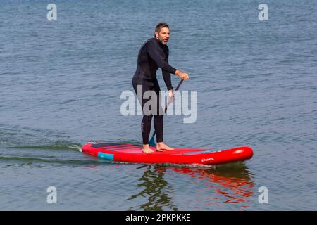 Sandbanks, Poole, Dorset, Großbritannien. 9. April 2023 Wetter im Vereinigten Königreich: Warm und sonnig im Sandbanks in Poole, wo leidenschaftliche Wassersportfreunde und -Enthusiasten ihre Aktivitäten im Sonnenschein auf dem Wasser genießen. Heute, der Ostersonntag, wird laut Prognose der heißeste Tag des Jahres bis jetzt sein, mit der Vorhersage von morgen Regen. Steh auf, Paddle Boarder. Kredit: Carolyn Jenkins/Alamy Live News Stockfoto