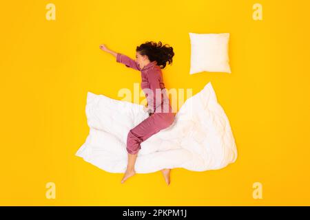 Eine Frau Schreit In Einem Schlafanzug, Sitzt Auf Einer Decke Über Gelbem Hintergrund Stockfoto