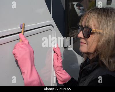 Eine attraktive weibliche Hand reinigt ihr Wohnmobil mit einer Zahnbürste. Sie trägt pinkfarbene Gummihandschuhe und eine Sonnenbrille. Zufrieden Stockfoto