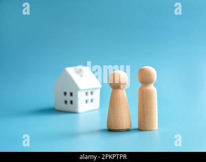 Liebespaar Holzfigur, männliches und weibliches Symbol, vor einem kleinen weißen Haus Miniatur auf blauem Hintergrund. Eine Familie aufbauen. Das erste Zuhause Stockfoto